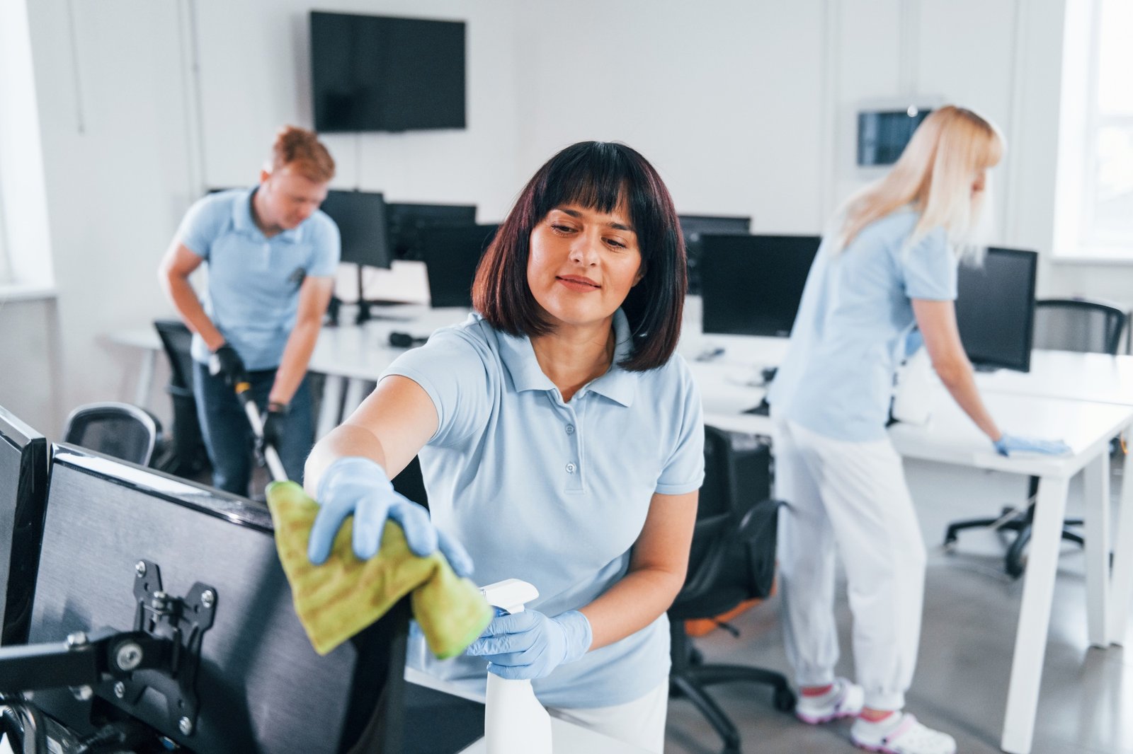 Cleans monitor. Group of workers clean modern office together at daytime